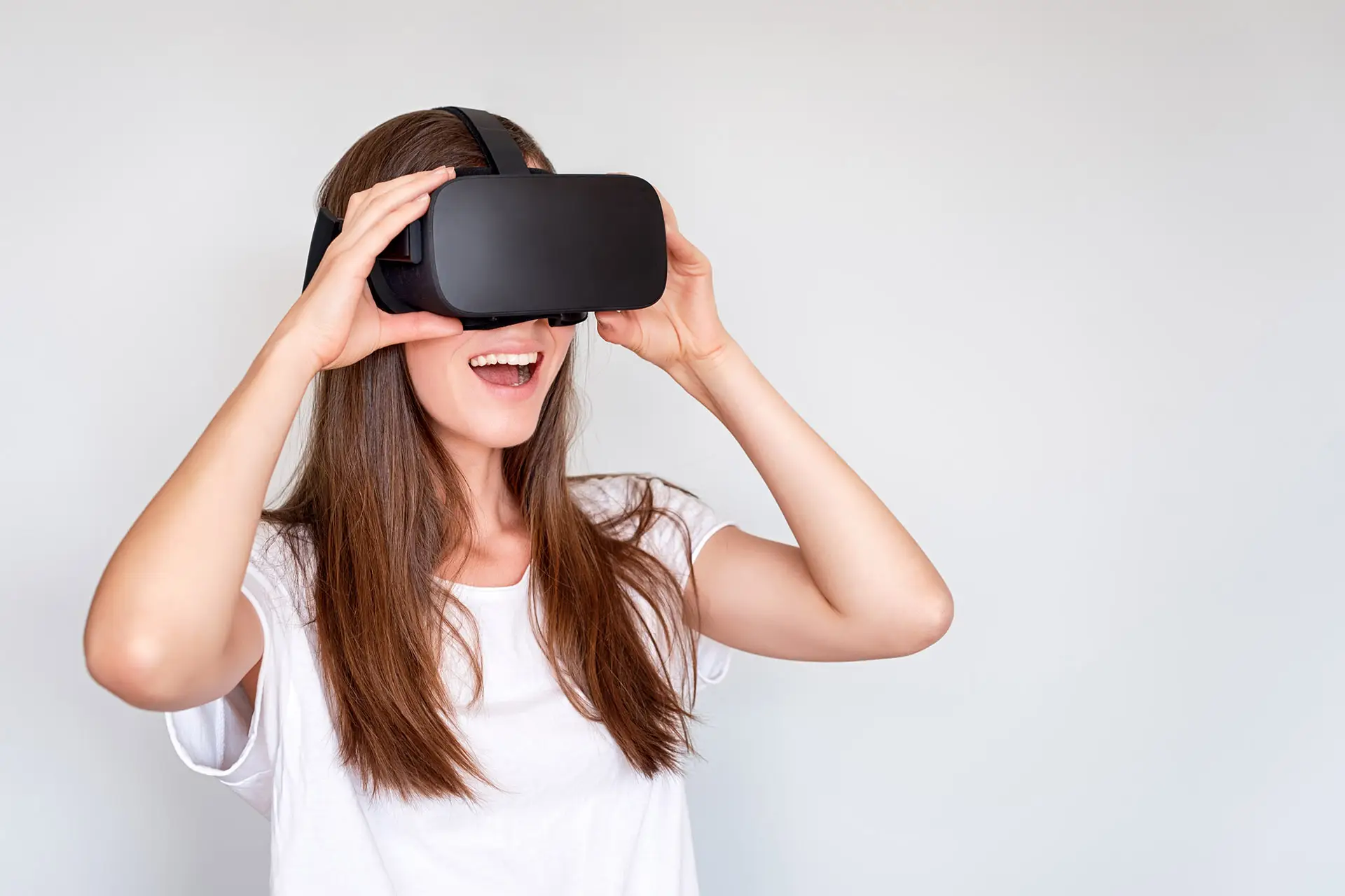 Lächelnde positive Frau mit Virtual-Reality-Brille, VR-Box. Verbindung, Technologie, neue Generation, Fortschrittskonzept. Mädchen versucht, Objekte in der virtuellen Realität zu berühren. Studioaufnahme auf Grau.