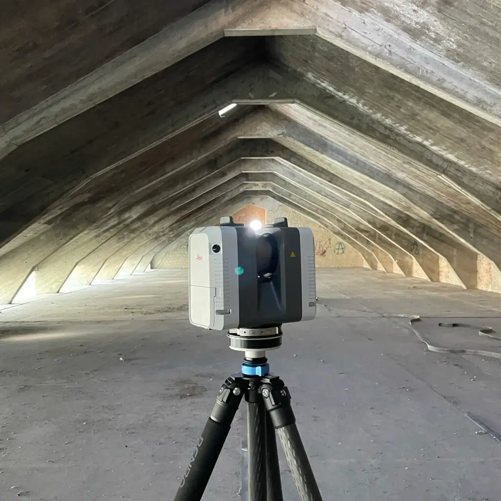 Ein Leica RTC360 Laserscanner in einem leerstehenden Dachgeschoss einer alten Indistriehalle. Die Dachkonstruktion ist wird von Stahlbeton-Streben getragen.